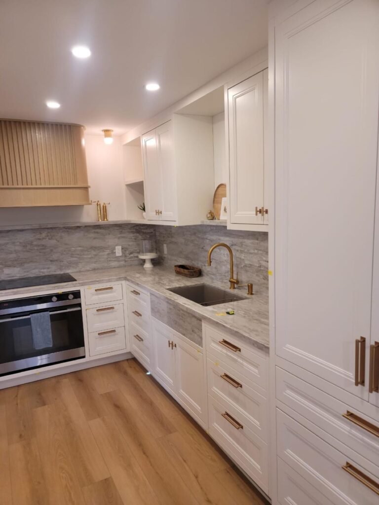 White kitchen cabinetry with brass hardware and stone backsplash by T.H. Cabinets