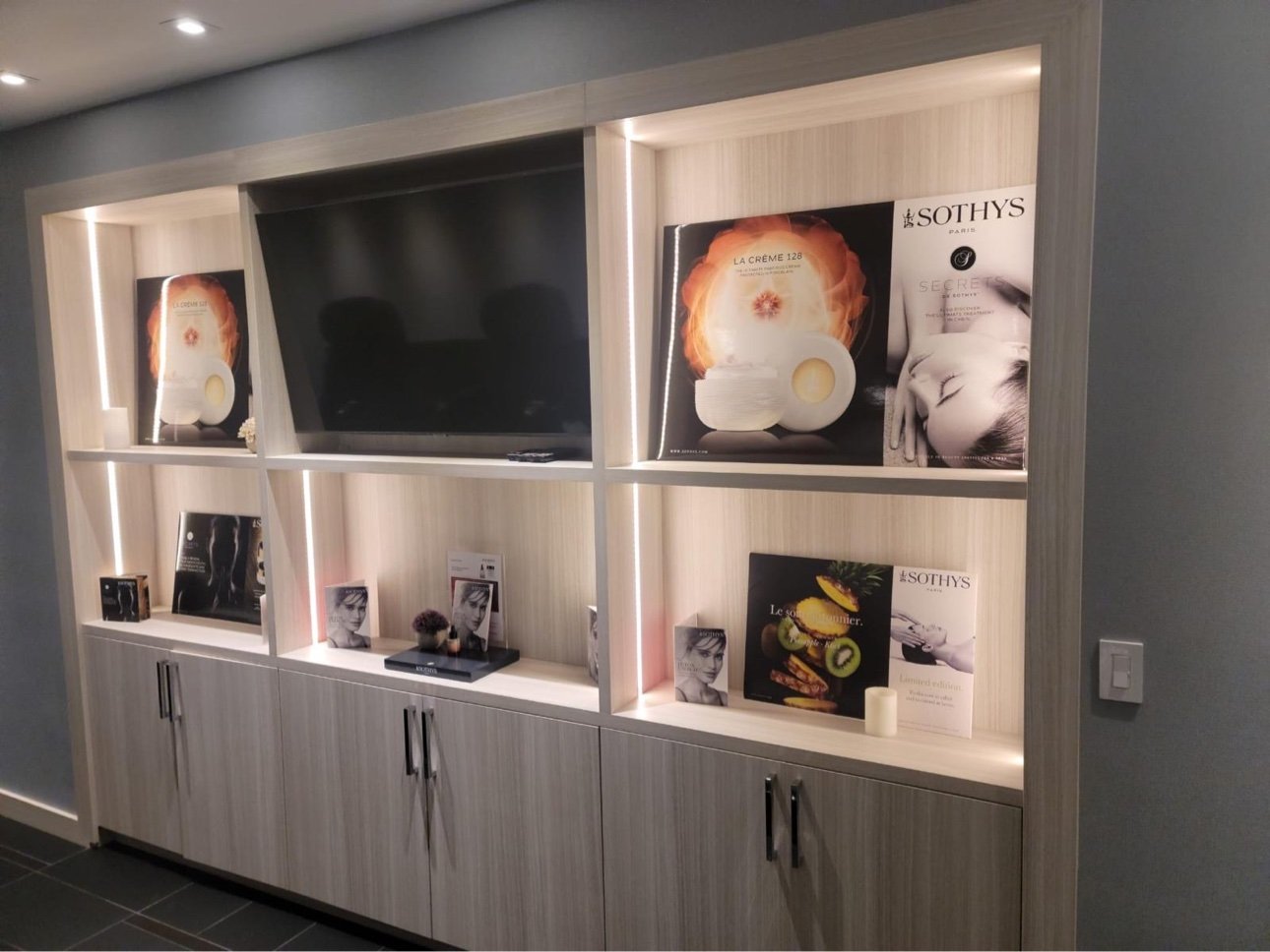 Backlit product display wall with integrated TV niche, salon millwork by T.H. Cabinets
