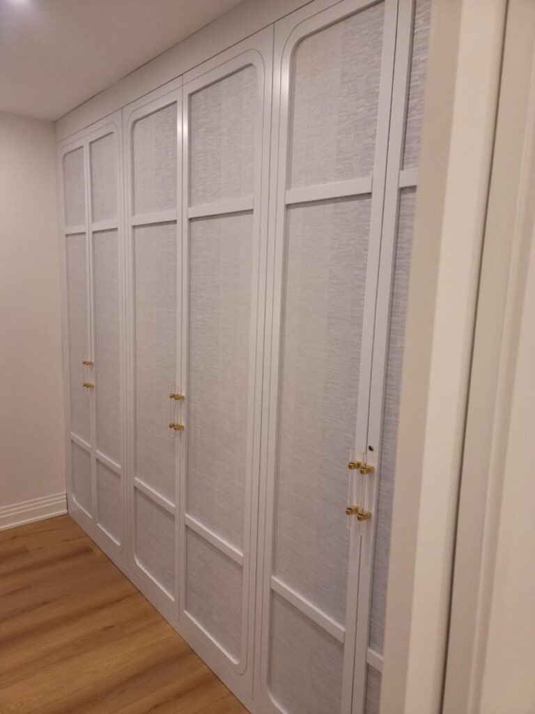 Floor-to-ceiling built-in wardrobe with textured panel doors by T.H. Cabinets