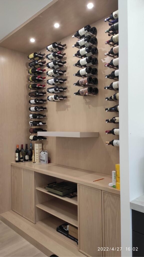 Custom oak wine display wall with pin racking and storage cabinets by T.H. Cabinets